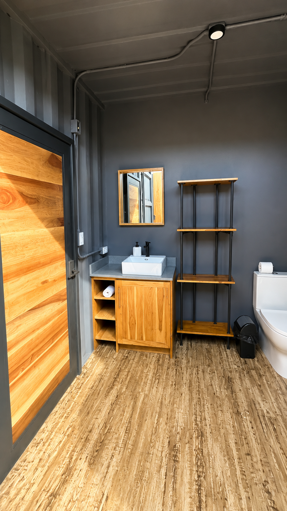 Bathroom vanity with teak cabinetry, vessel sink and open shelving next to a sliding wood door