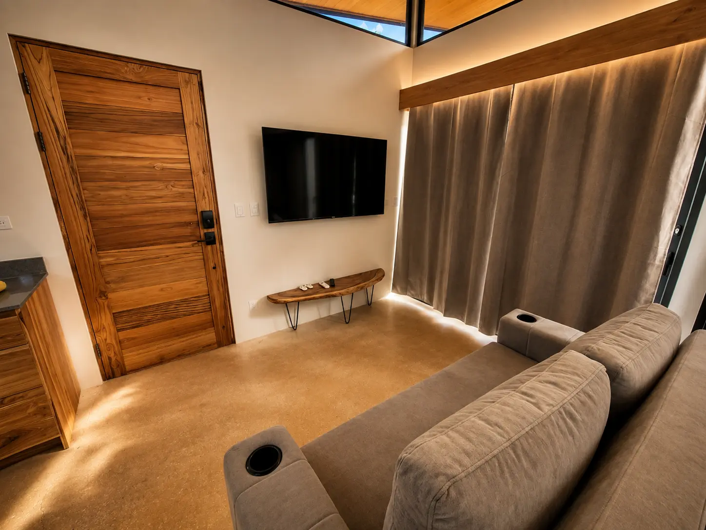 Living area with sofa, Smart TV and teak entry door under warm evening light