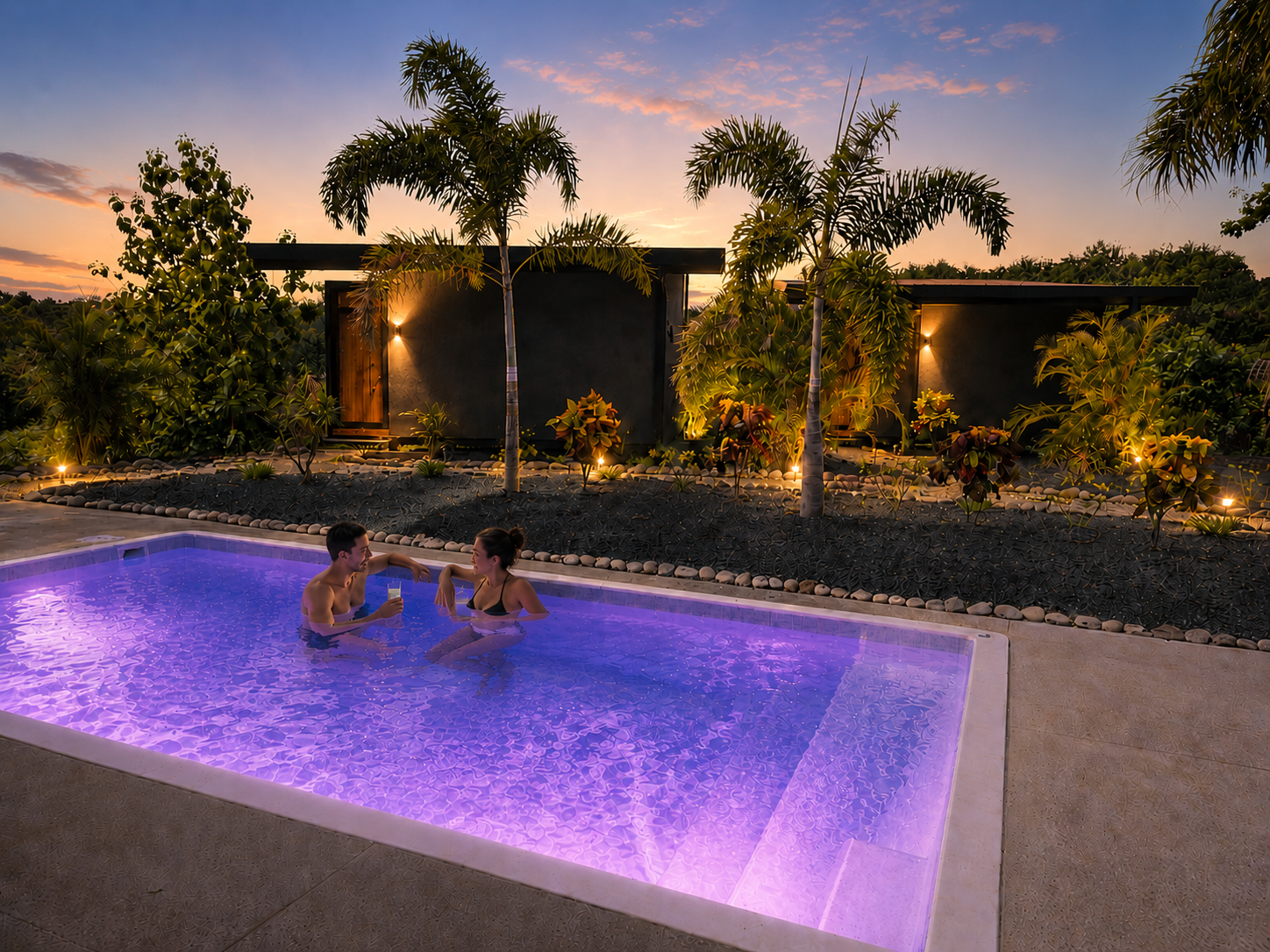 Couple relaxing in the illuminated pool at sunset with the bungalows behind