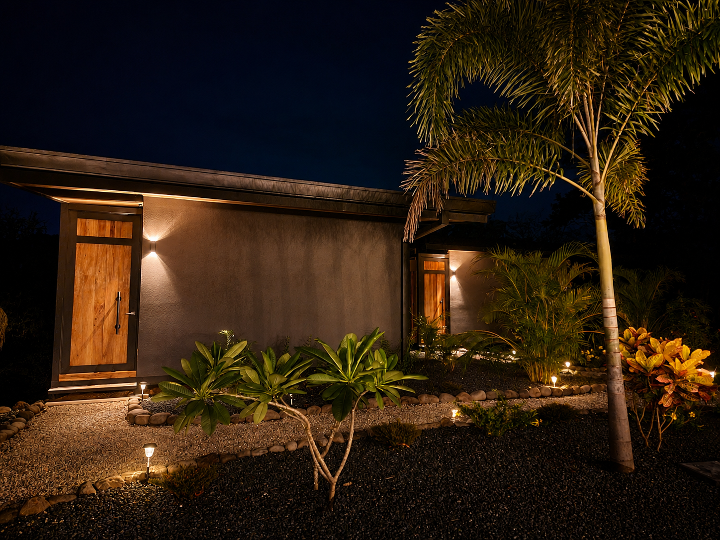 Bungalows warmly lit at night with landscape lighting, palms and wooden entry doors
